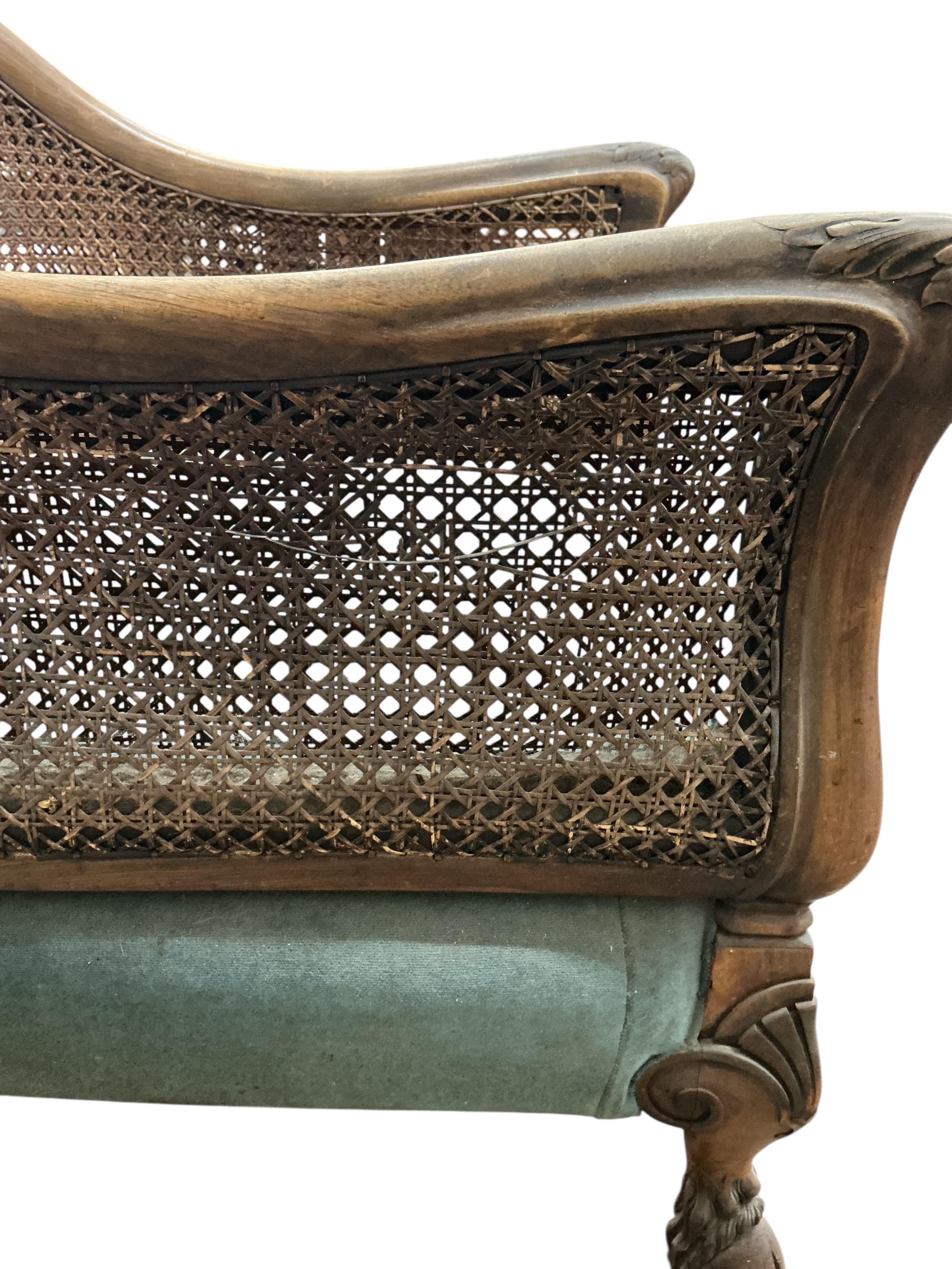 An early 20th century carved walnut and double canework three piece bergère suite, cane in need of repair